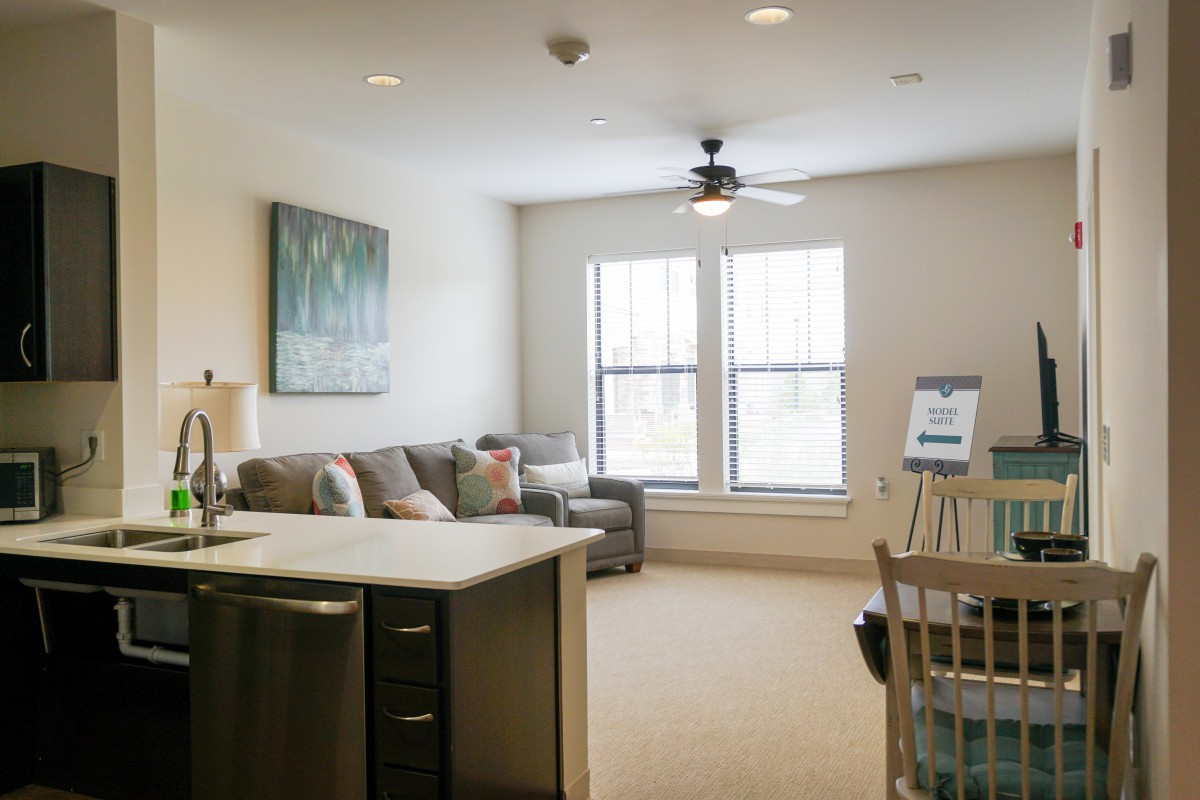 A bright and cozy living room with modern decor, featuring a large sofa, ceiling fan, and ample natural light from two windows.