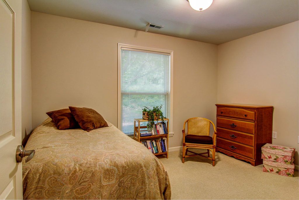 A cozy bedroom with a bed, chair, and dresser, featuring natural light from the window.