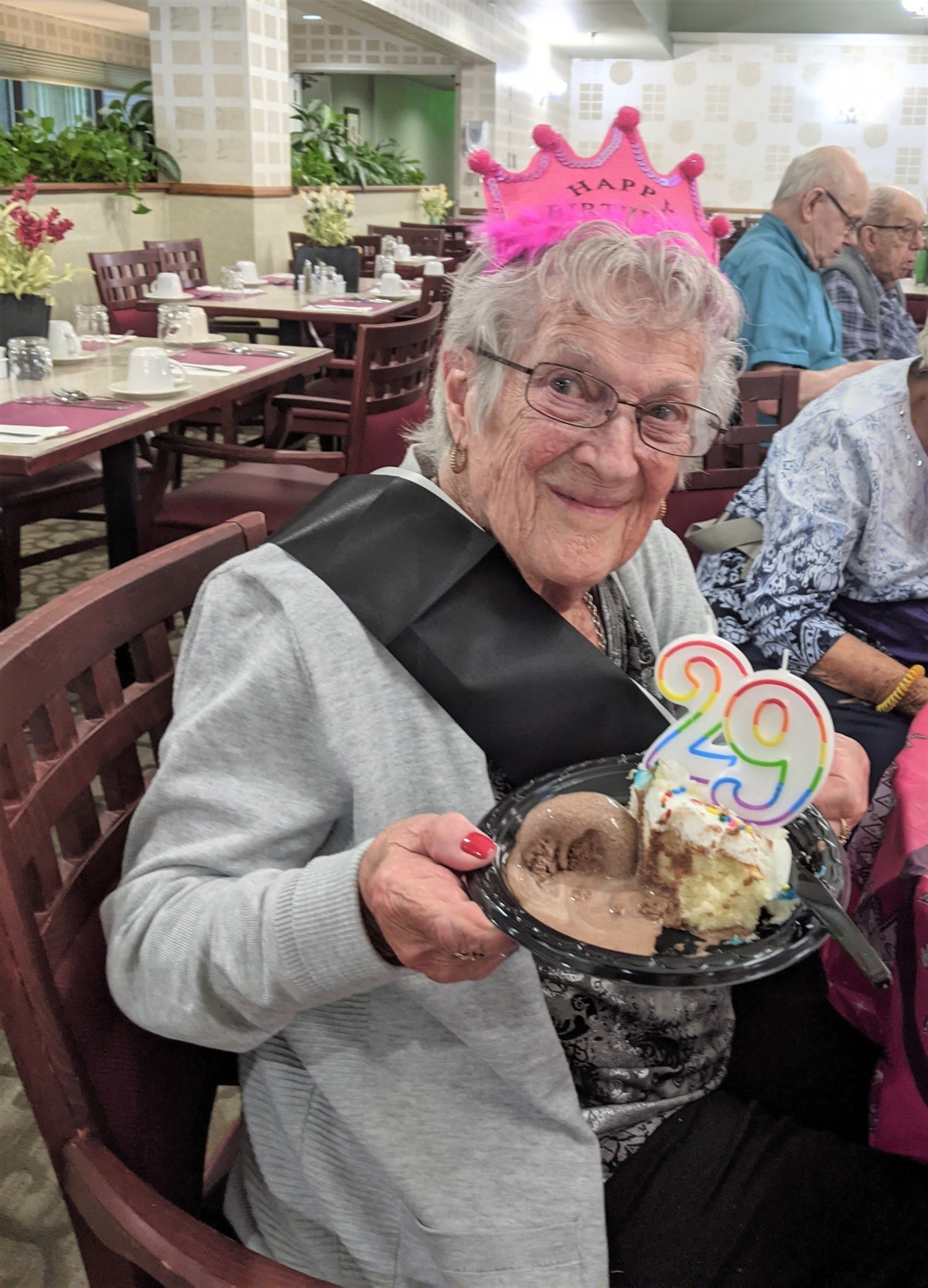 An elderly person celebrating their birthday with a slice of cake, wearing a party hat and smiling.