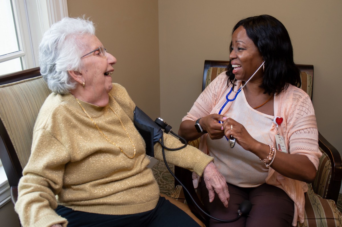 A healthcare worker smiling while checking an elderly woman's blood pressure.