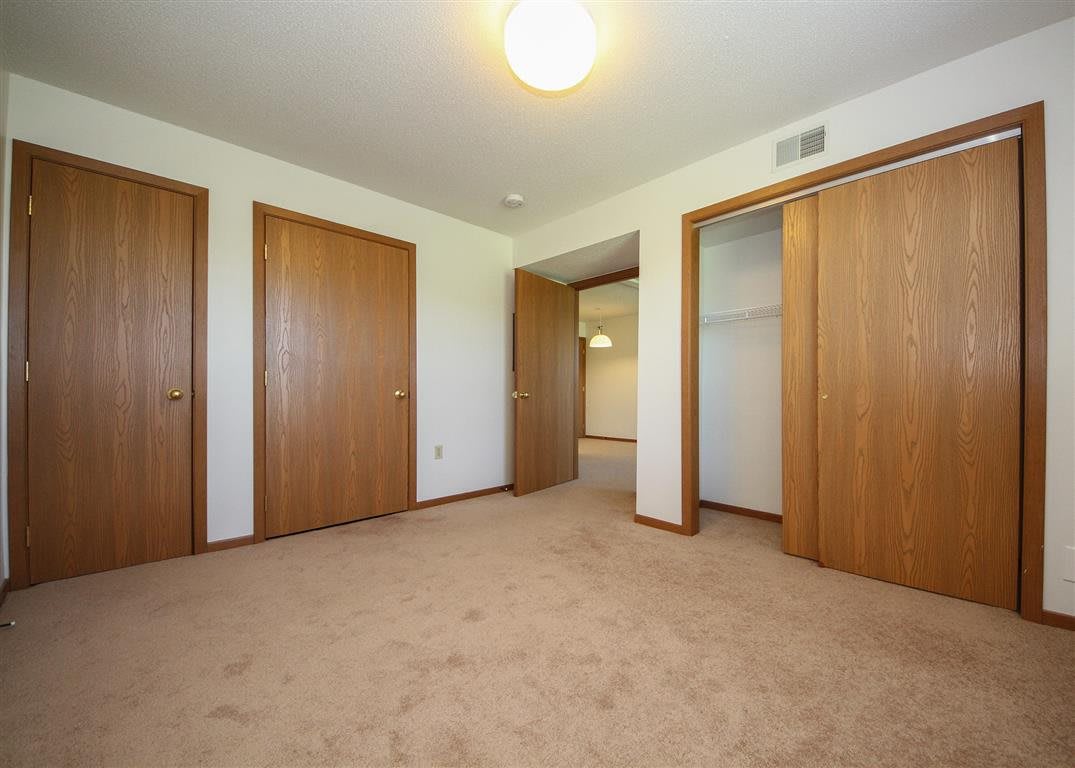An empty bedroom with carpet flooring, wooden closet doors, and a ceiling light.