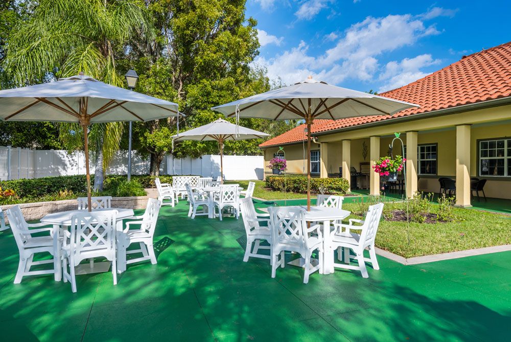 A sunny outdoor patio area with white tables and umbrellas set on a green surface.
