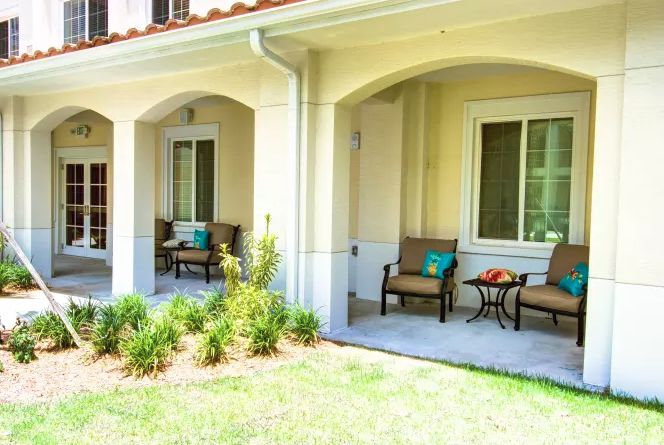 A cozy patio area with comfortable chairs and a small table, surrounded by greenery.