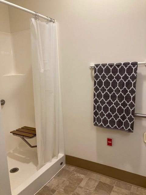 A bathroom with a shower featuring a curtain and a wooden bench, alongside a towel hanging on the wall.