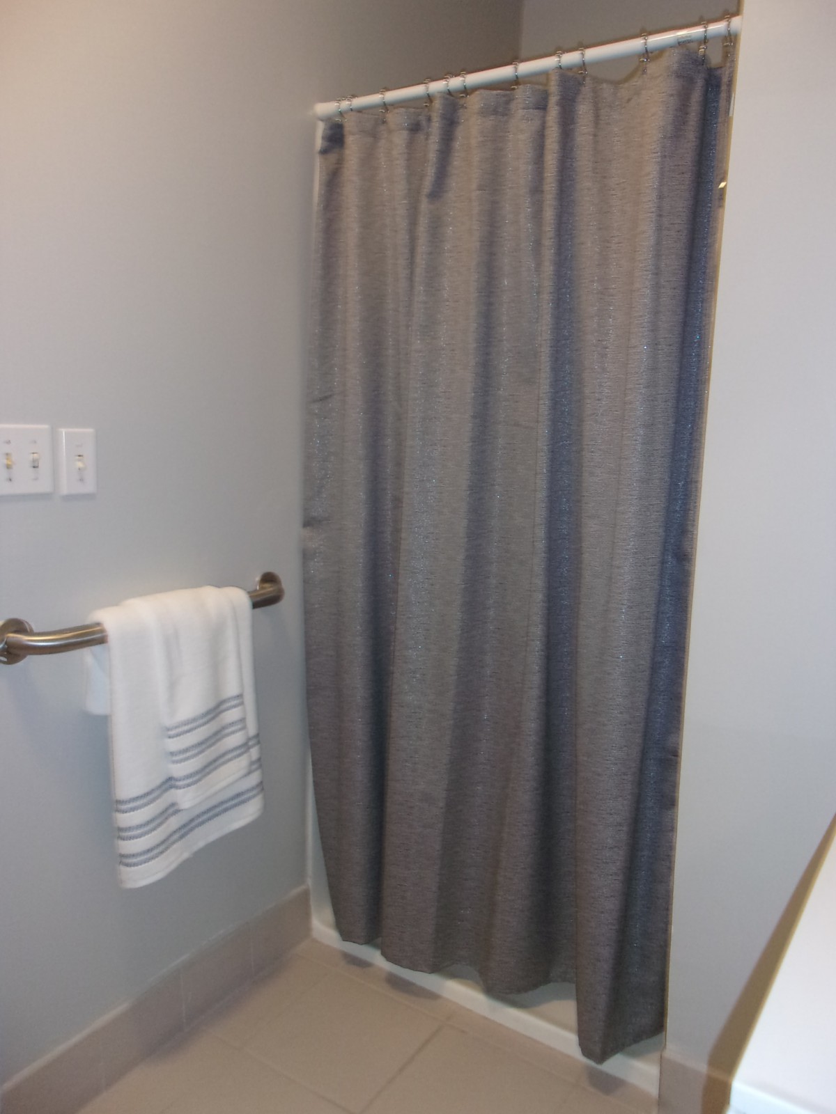 A bathroom with a gray shower curtain and a towel hanging on a bar.