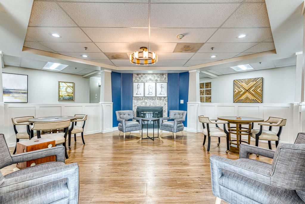 A modern living room with elegant furniture and a central chandelier, featuring a seating area and wooden flooring.