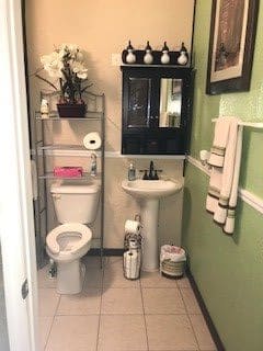 A compact bathroom with a sink, toilet, and shelving unit, featuring green walls and decorative accents.