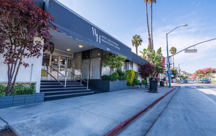 A view of a modern building entrance with palm trees lining the street.