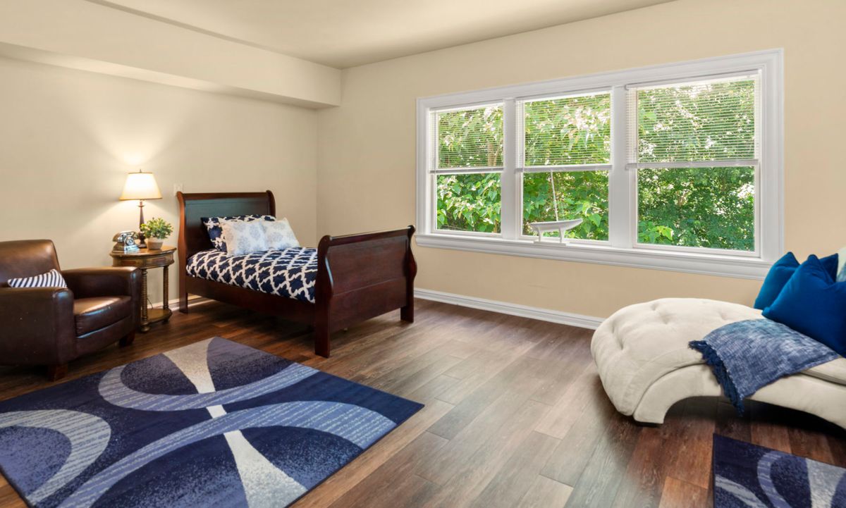 A minimalistic bedroom with a single bed, large window, and wooden flooring.