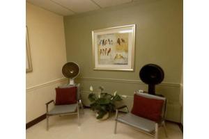 A small waiting area with two chairs, each equipped with a hair dryer, a framed artwork on the wall, and a potted plant on the floor.