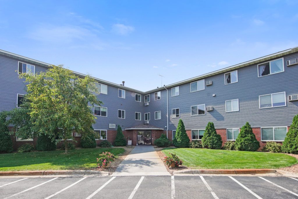 A three-story residential apartment building with a parking lot and landscaped greenery.