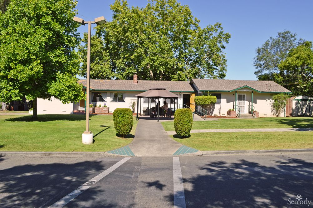 A single-story building with a pathway leading up to it, surrounded by trees and bushes on a sunny day.