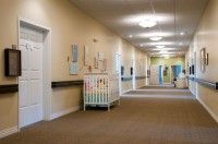 A long institutional hallway featuring a crib and multiple doors.