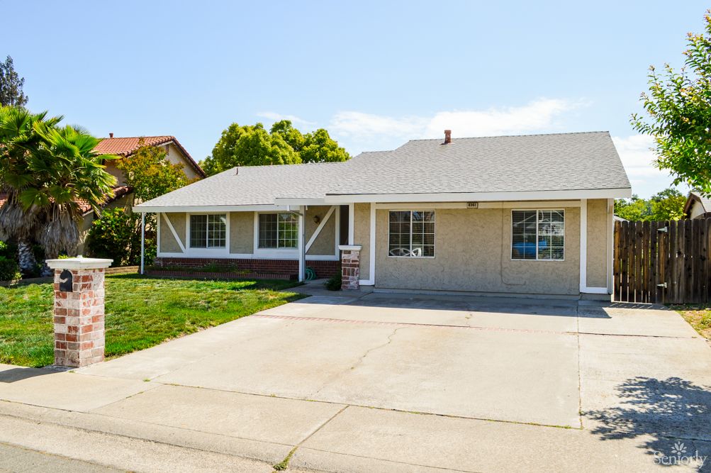 A suburban single-story house with a spacious driveway and front yard.