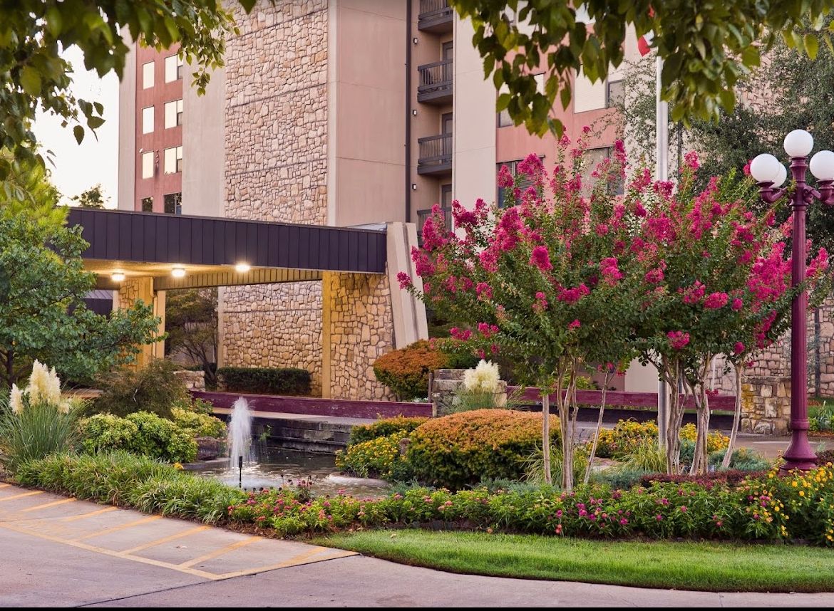 A beautifully landscaped hotel entrance featuring a small fountain and vibrant flowers.