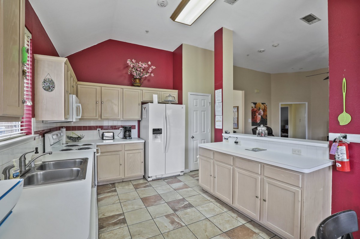 A modern kitchen with white cabinets, a red accent wall, and tile flooring.