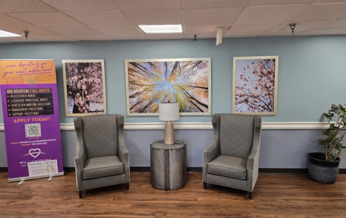 A cozy waiting area with two gray armchairs flanking a small round table, set against a wall adorned with abstract artwork.