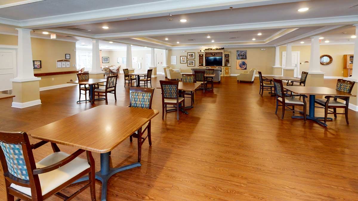 A spacious dining room with wooden floors, tables, and chairs arranged neatly under ceiling lights.