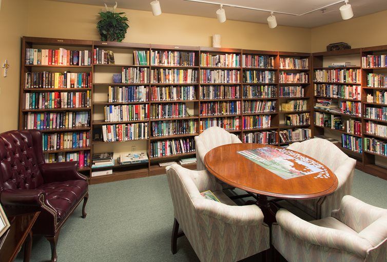 A cozy library reading area with bookshelves, a round table, and comfortable chairs.