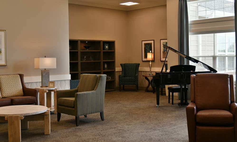 A cozy lounge area featuring a piano, armchairs, and bookshelves.