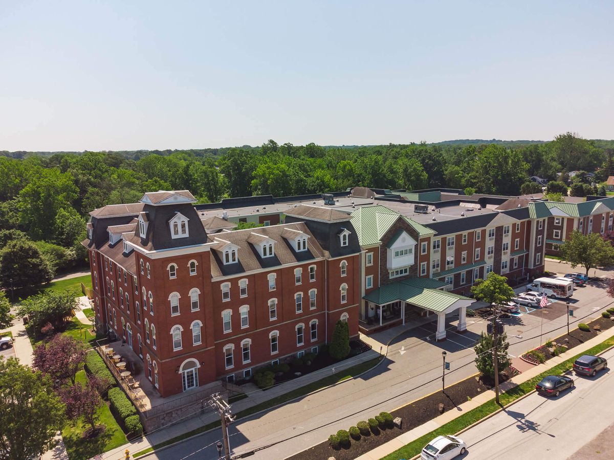 Aerial view of a historic red brick hotel with a parking lot surrounded by trees on a sunny day.