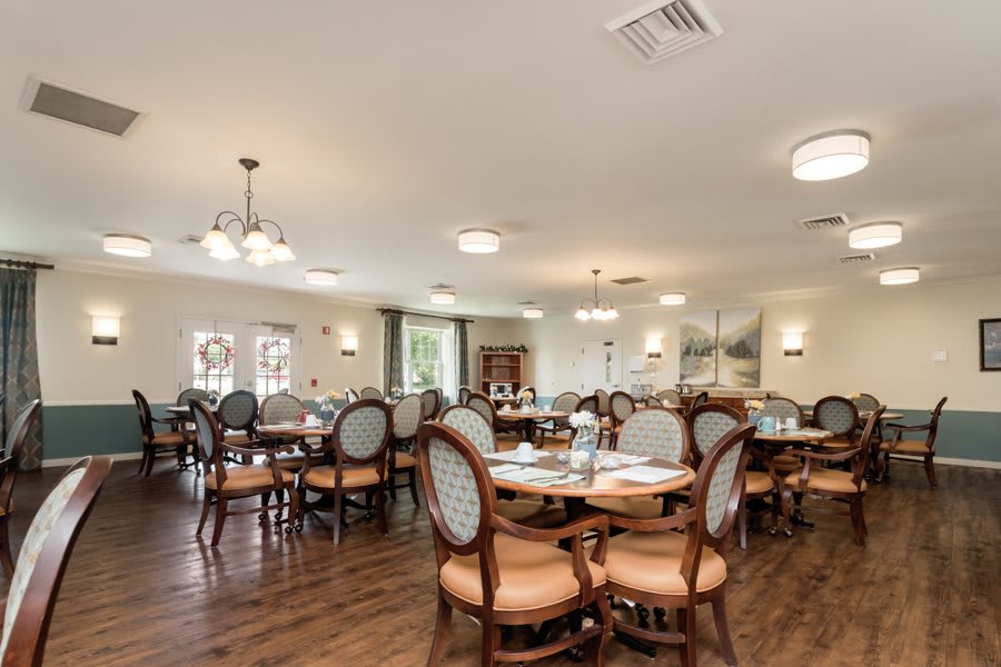 A spacious and elegantly furnished dining room with multiple tables and chairs, featuring warm lighting and a wooden floor.