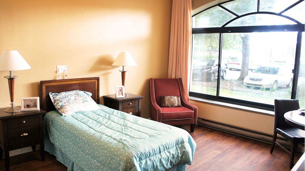 A cozy bedroom with a single bed, a bedside table, and a large window.