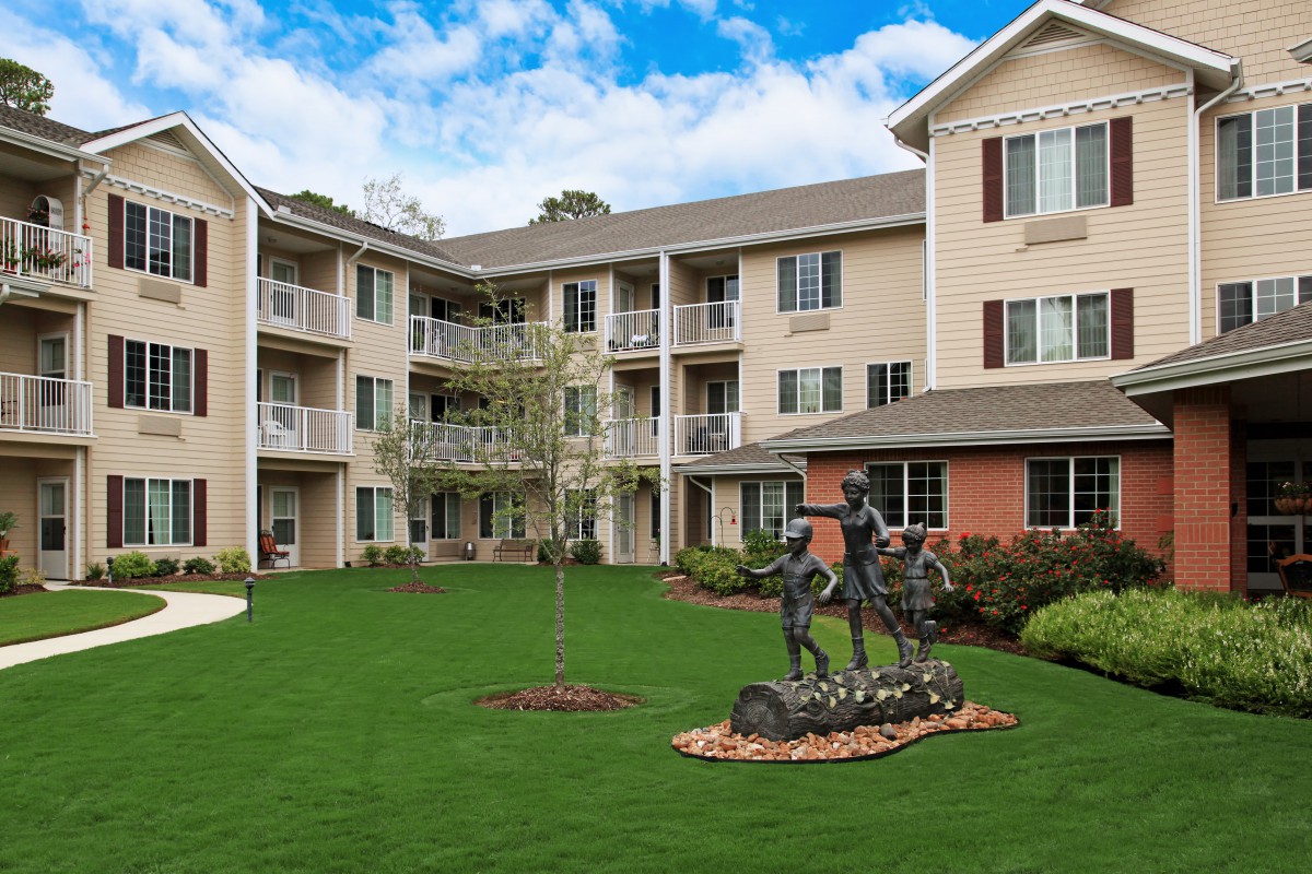 A well-maintained residential apartment building with a green lawn and sculpture in the courtyard.