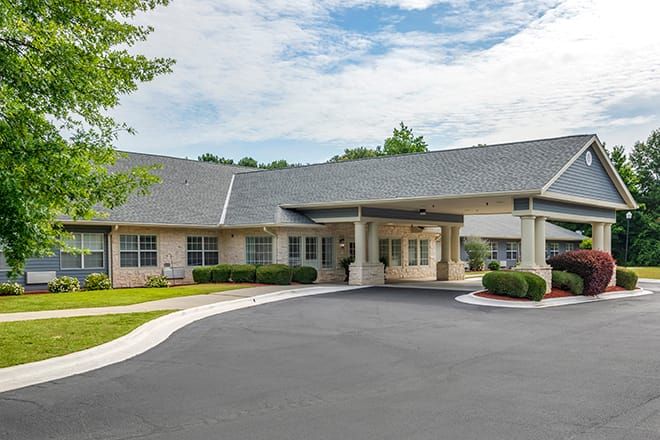 A building with a driveway and entrance surrounded by trees under a partly cloudy sky.