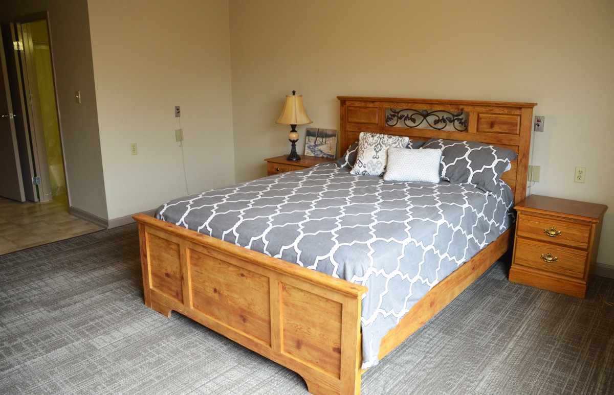 A cozy bedroom with a wooden bed, patterned bedding, and a bedside lamp.