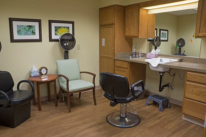A well-equipped salon room with a hair dryer, chairs, sink, and mirror.
