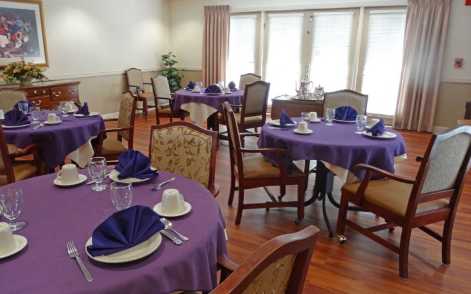 A well-set dining area with tables covered in purple tablecloths, complete with place settings and seating.