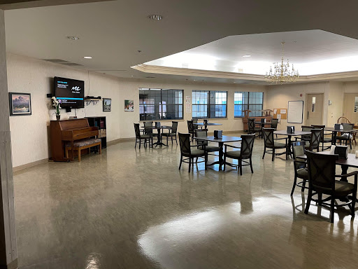 A spacious dining area with tables and chairs arranged for guests, featuring a television and ample natural light.