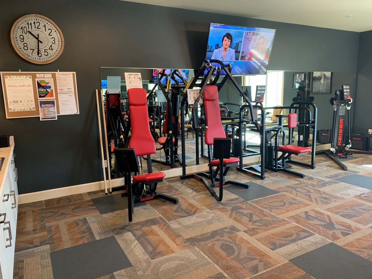 A gym area with exercise equipment, mirrors, a TV, and a wall clock.