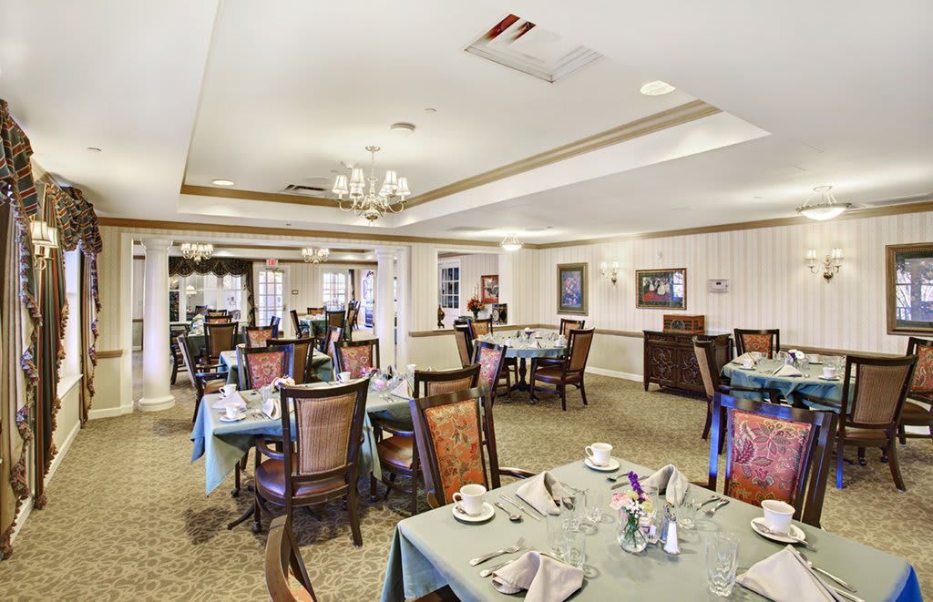 An elegant dining room with neatly arranged tables and chairs, featuring a chandelier and tasteful decor.