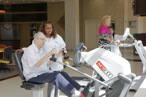 A caregiver assists a senior individual using exercise equipment for rehabilitation.