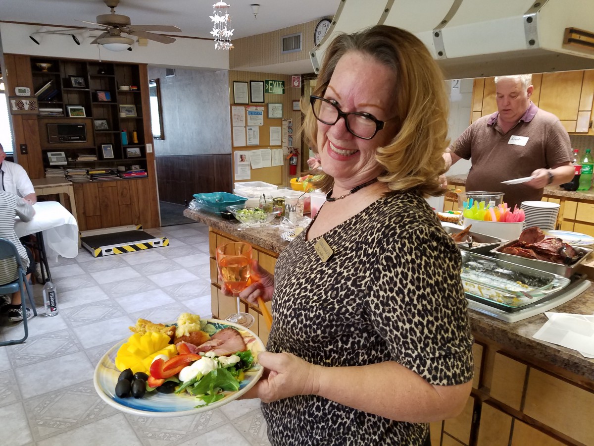 A woman holding a plate of food at a buffet, smiling at the camera.