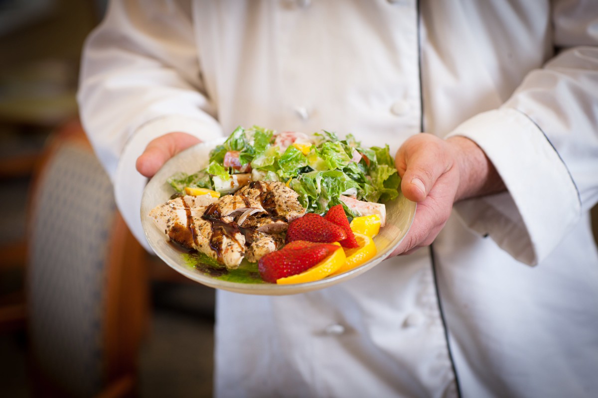 A chef presents a fresh salad with grilled chicken and vibrant vegetables.