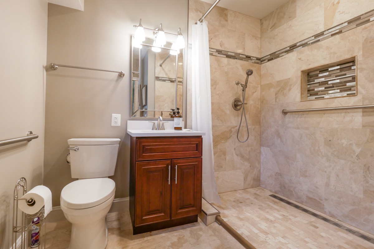 A modern bathroom with a wooden vanity, walk-in shower, and tile flooring.