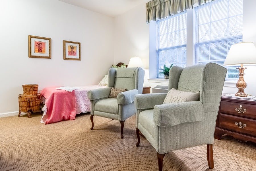A cozy living room with two armchairs, a bed, and large windows.