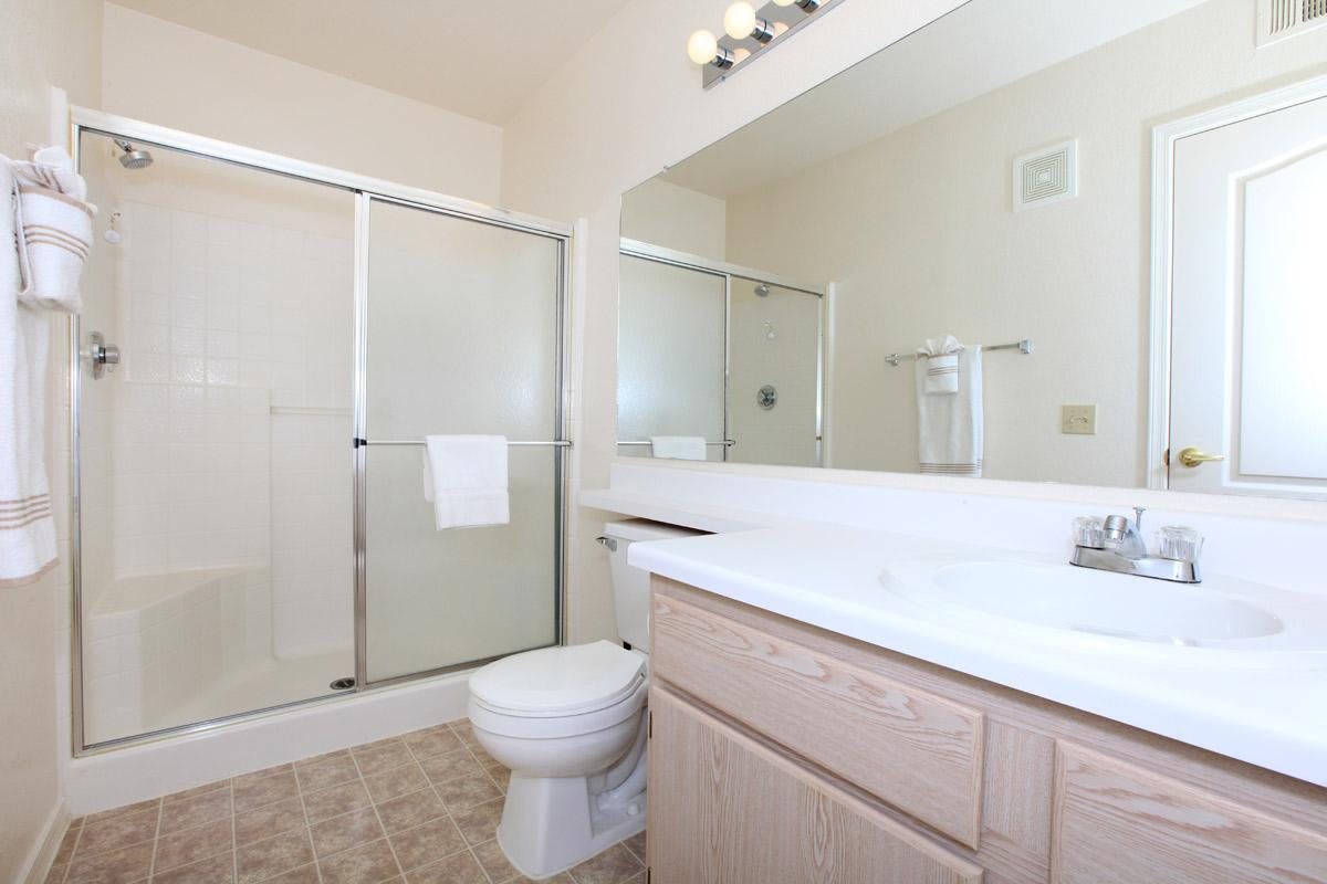 A clean and bright bathroom with a shower, toilet, sink, and mirror.