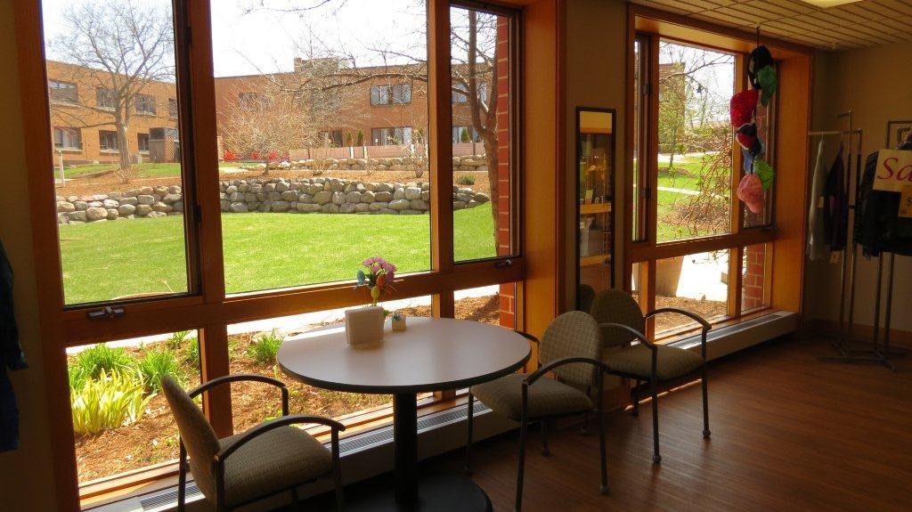 A cozy cafe interior with a round table and chairs by a large window overlooking a green outdoor area.