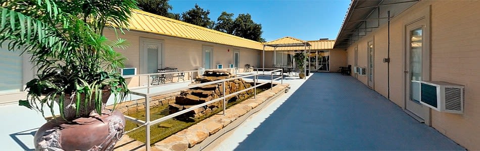 A sunny outdoor area featuring a ramp with handrails, rocks, and a building with a yellow roof.