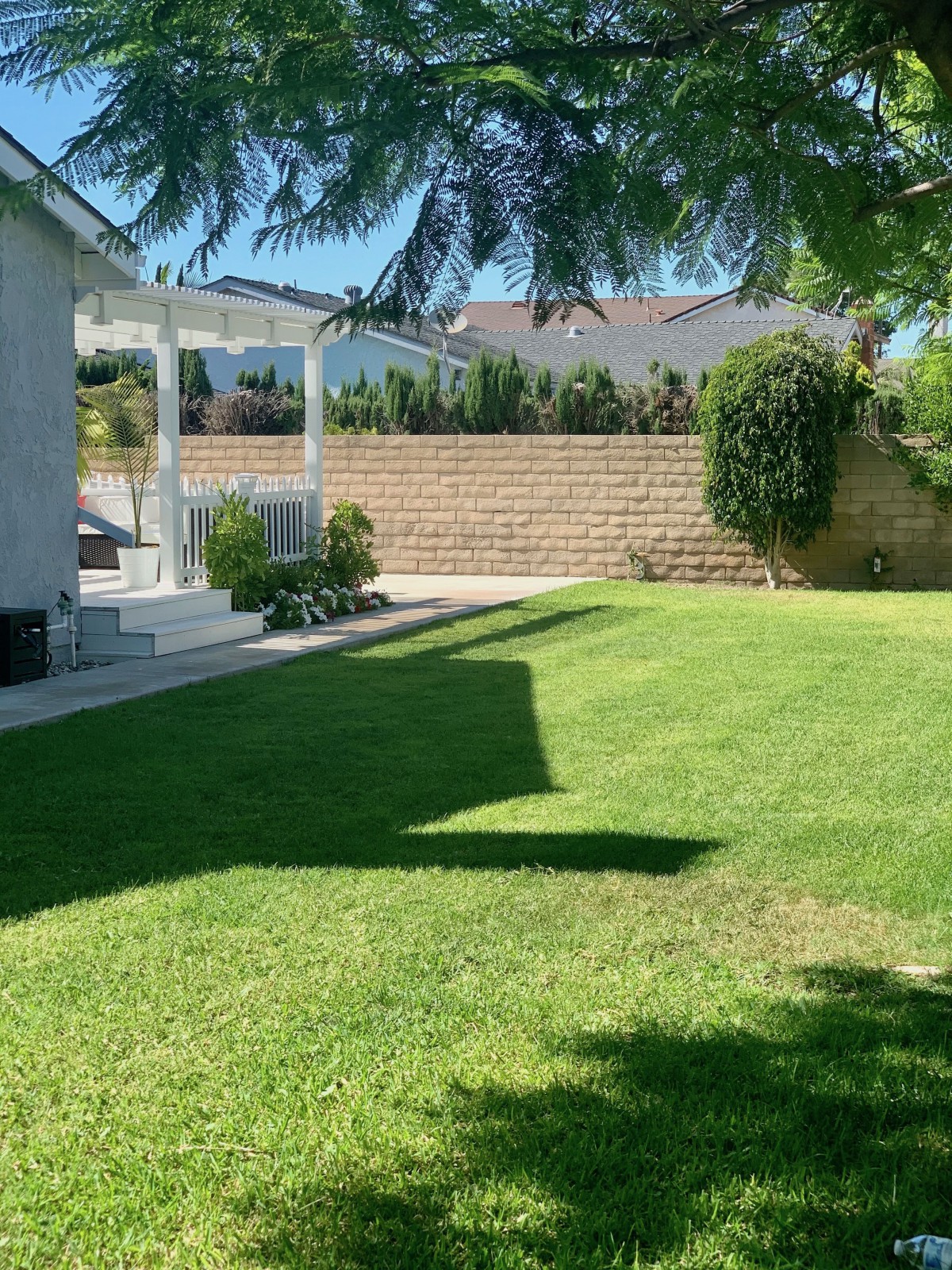 A sunny backyard with a lush green lawn and a covered patio.