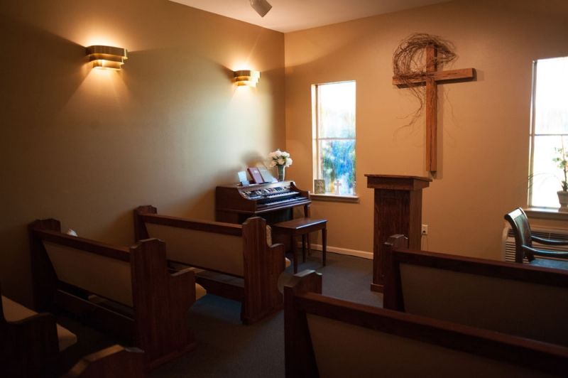 A small chapel interior featuring wooden pews, a pulpit, an organ, and a cross on the wall.