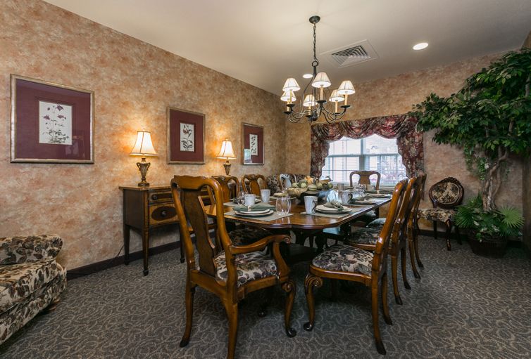 A traditional dining room with a large wooden table set for a meal, featuring ornate chairs and a central chandelier.
