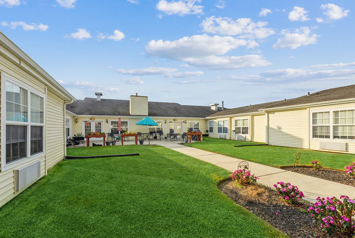 A sunny courtyard with a vibrant green lawn and outdoor seating areas, surrounded by a one-story building.