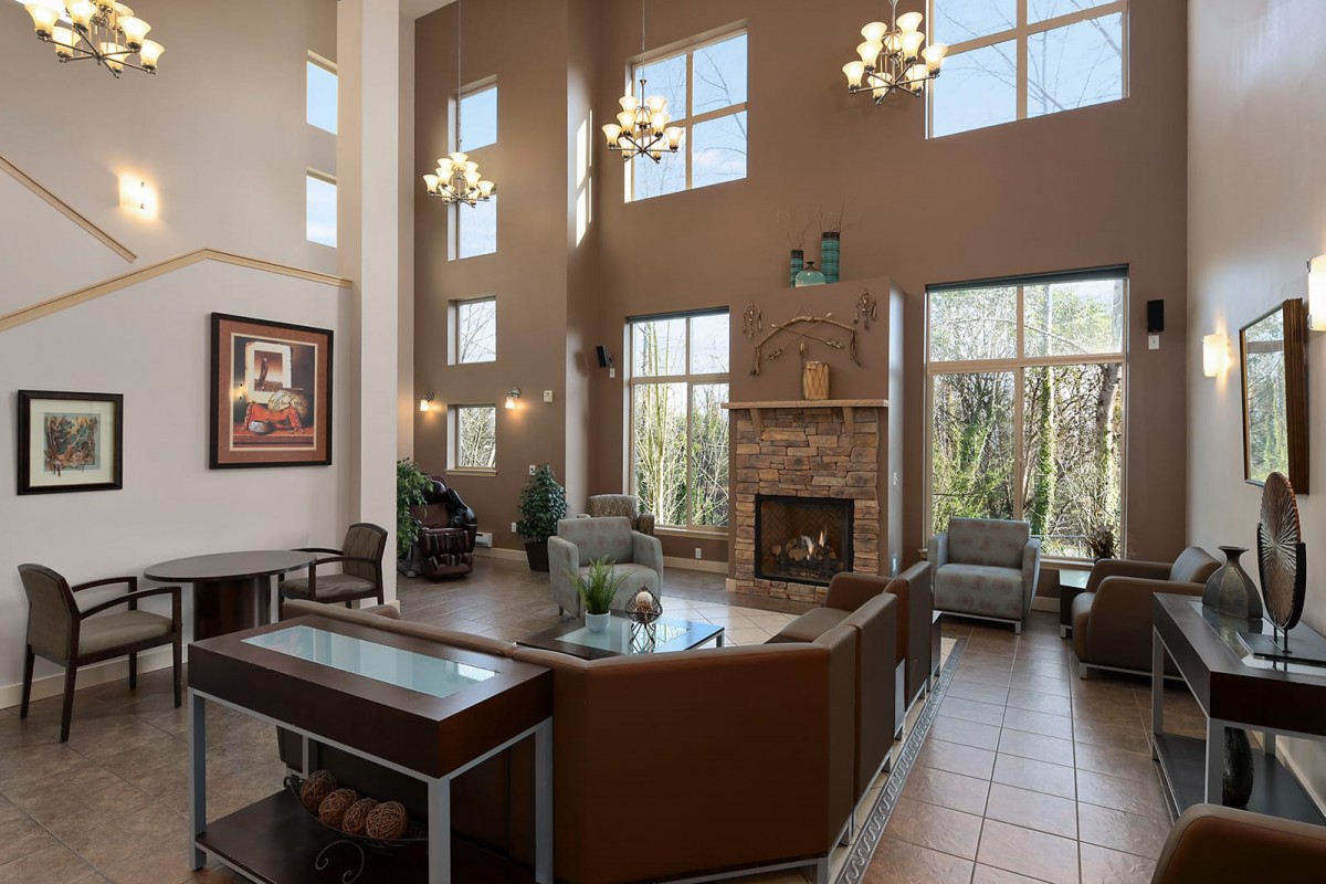 A modern lobby with high ceilings, chandeliers, and a cozy fireplace surrounded by a seating area.