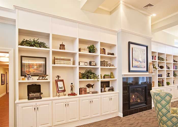 A warmly lit living room with a white bookshelf and fireplace, adorned with various decorative items.