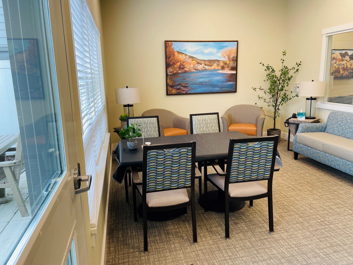 A cozy meeting room with a table and chairs, decorated with artwork, lamps, and an indoor plant.